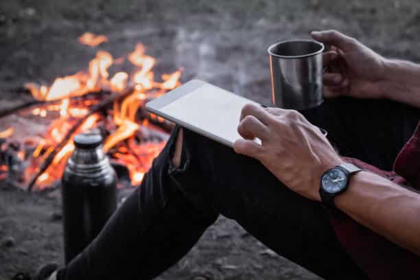 Camper at an RV park using a tablet near the fire. Wi-Fi is a deciding factor for 54% of campers when they choose a park to stay at. 